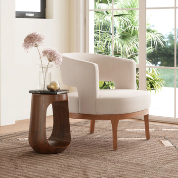 White armchair and wooden side table in a room with large windows and plants.
