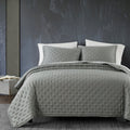 Gray quilted bedding set on a bed against a dark wall.