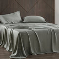 Gray satin sheet set on a bed with a wooden headboard.