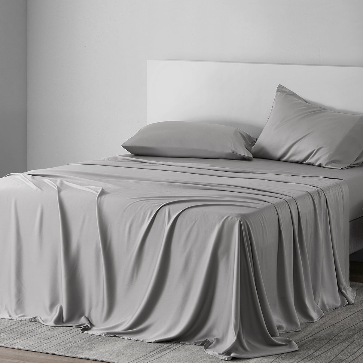 Gray bed sheets and pillows on a bed in a minimalistic bedroom.
