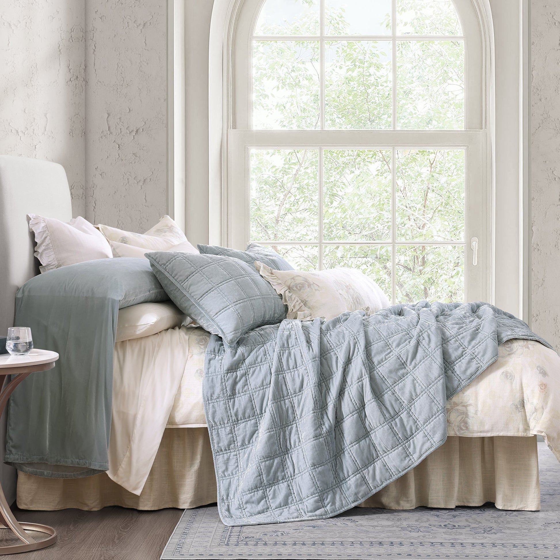 Bed with light blue quilt and pillows in a bright bedroom