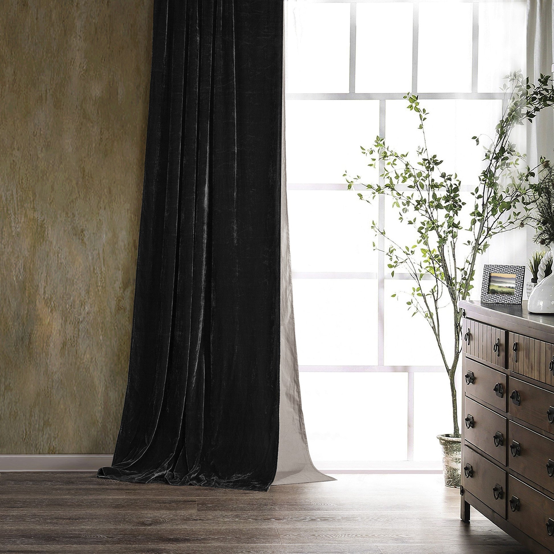 Black curtain in a room with a wooden dresser and plant