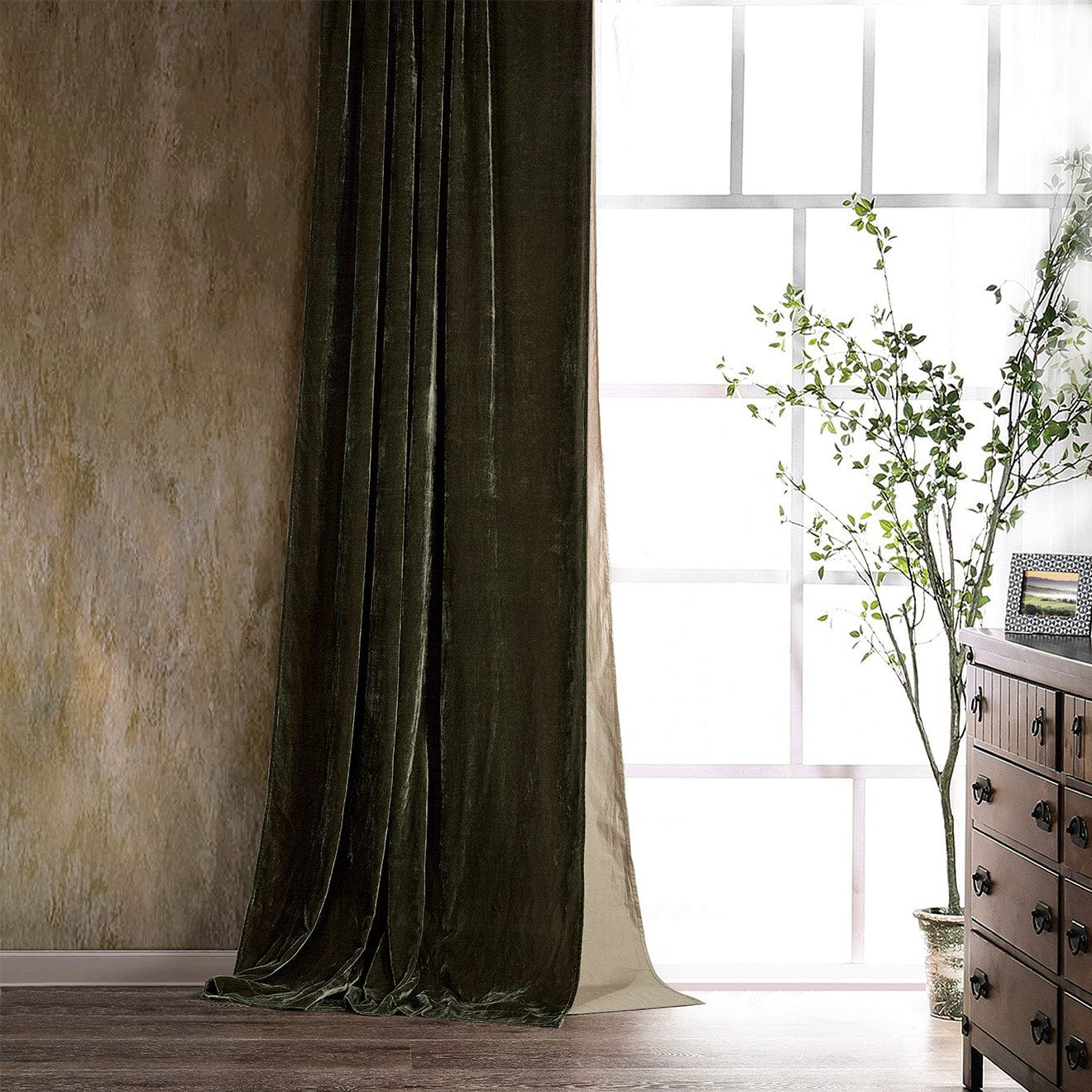 Dark green curtain in front of a window with a wooden dresser and plant in the background.