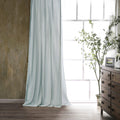 Light blue curtain in a room with a wooden dresser and plant