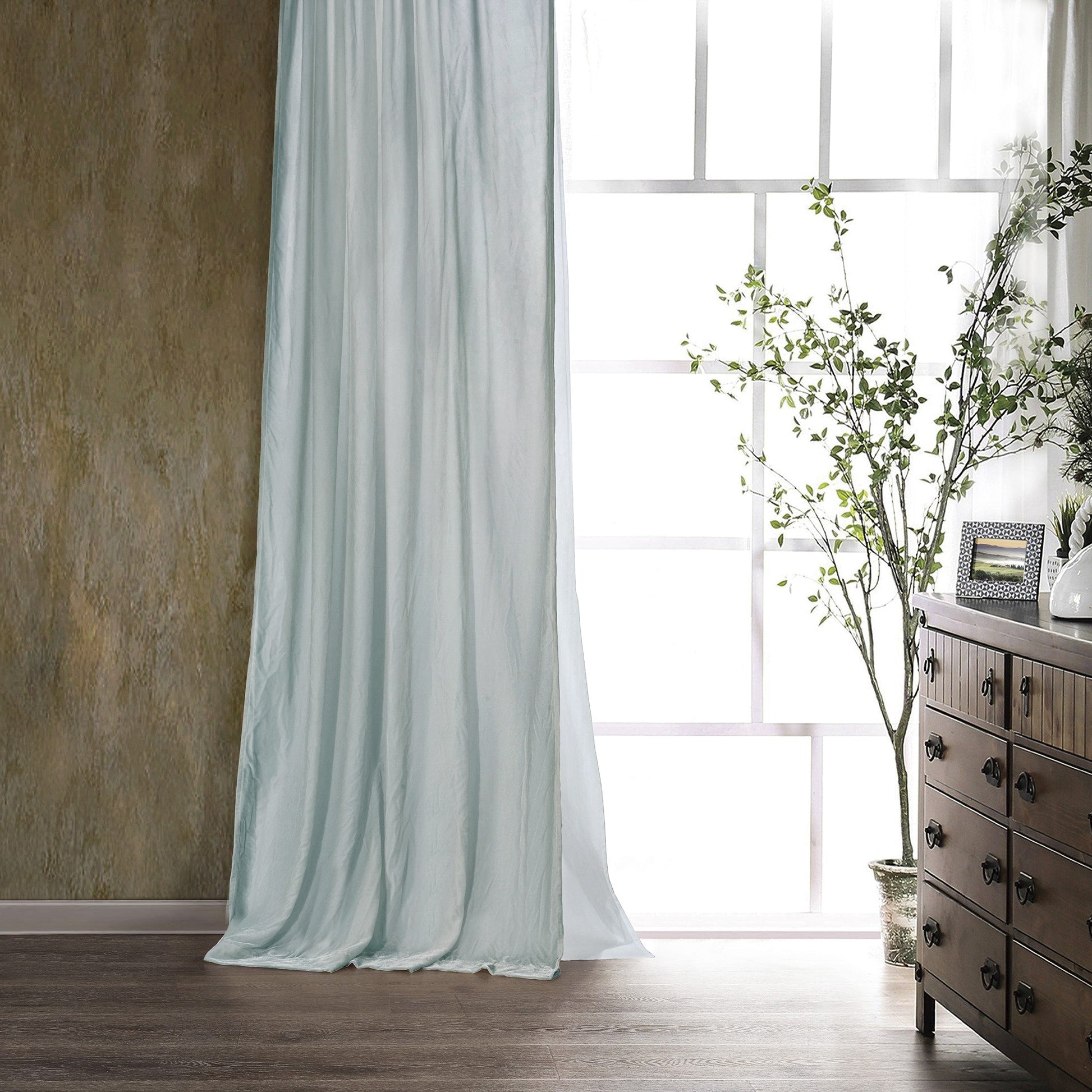 Light blue curtain in a room with a wooden dresser and plant
