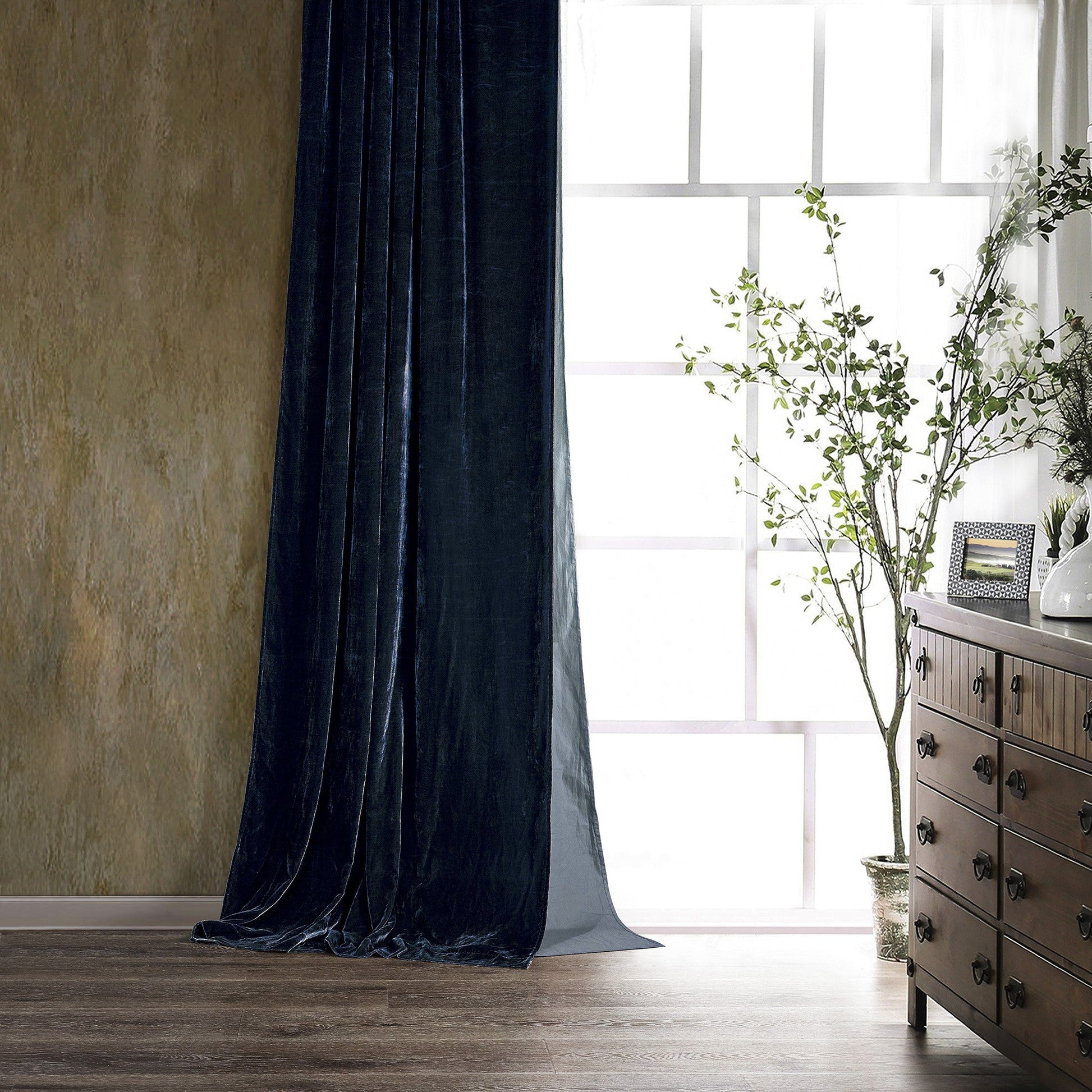 Dark blue curtain in a room with a wooden dresser and plant