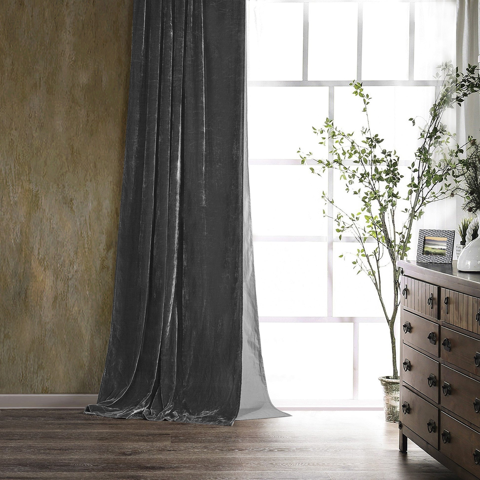 Dark gray curtain in a room with a wooden dresser and plant