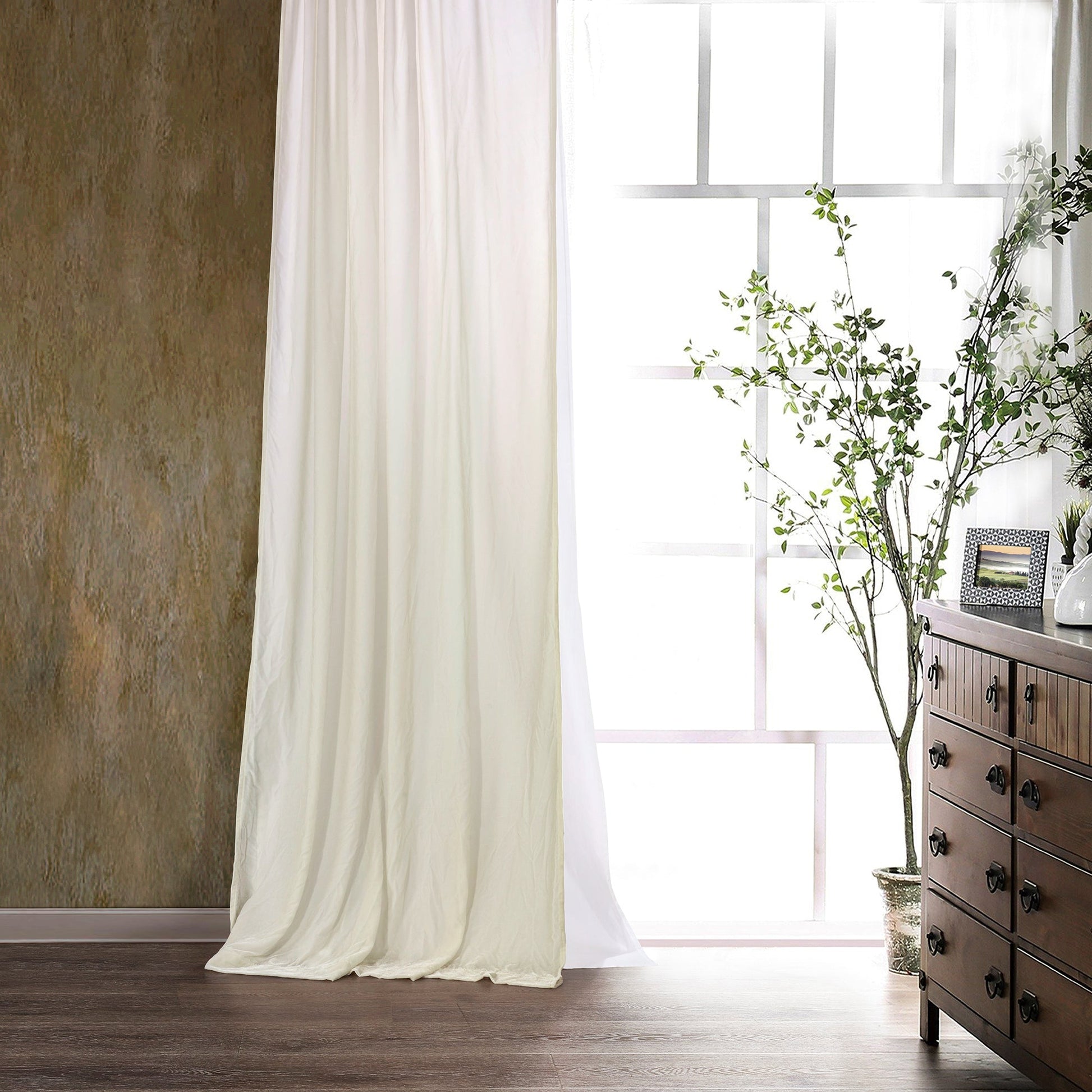 White curtains hanging in a room with a wooden dresser and decorative items.