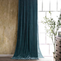 Teal velvet curtain in a room with a wooden dresser and window.