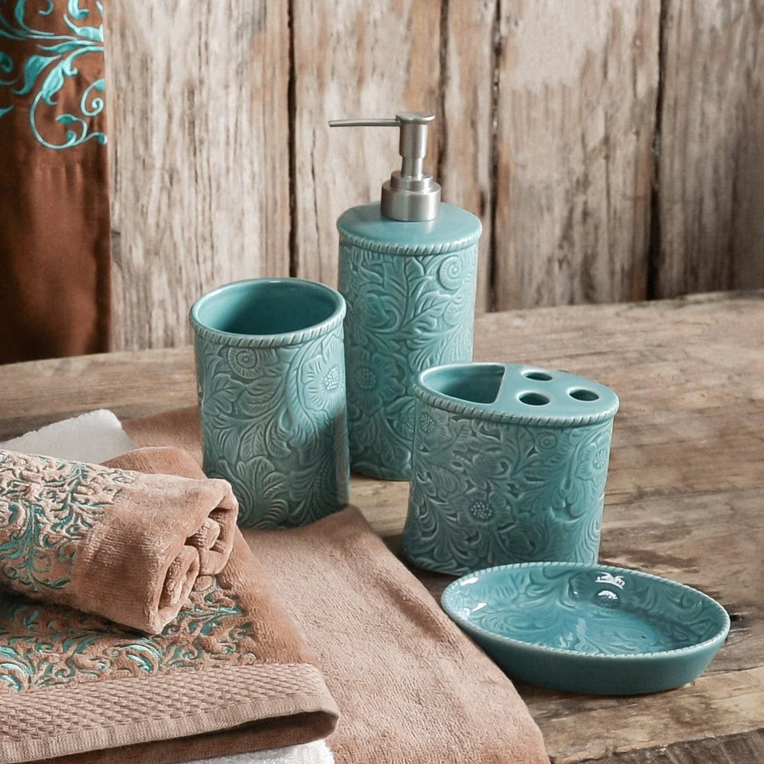 Teal bathroom accessories set on a wooden surface with towels.