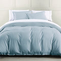 Blue comforter set on a bed with white pillows against a light gray wall.