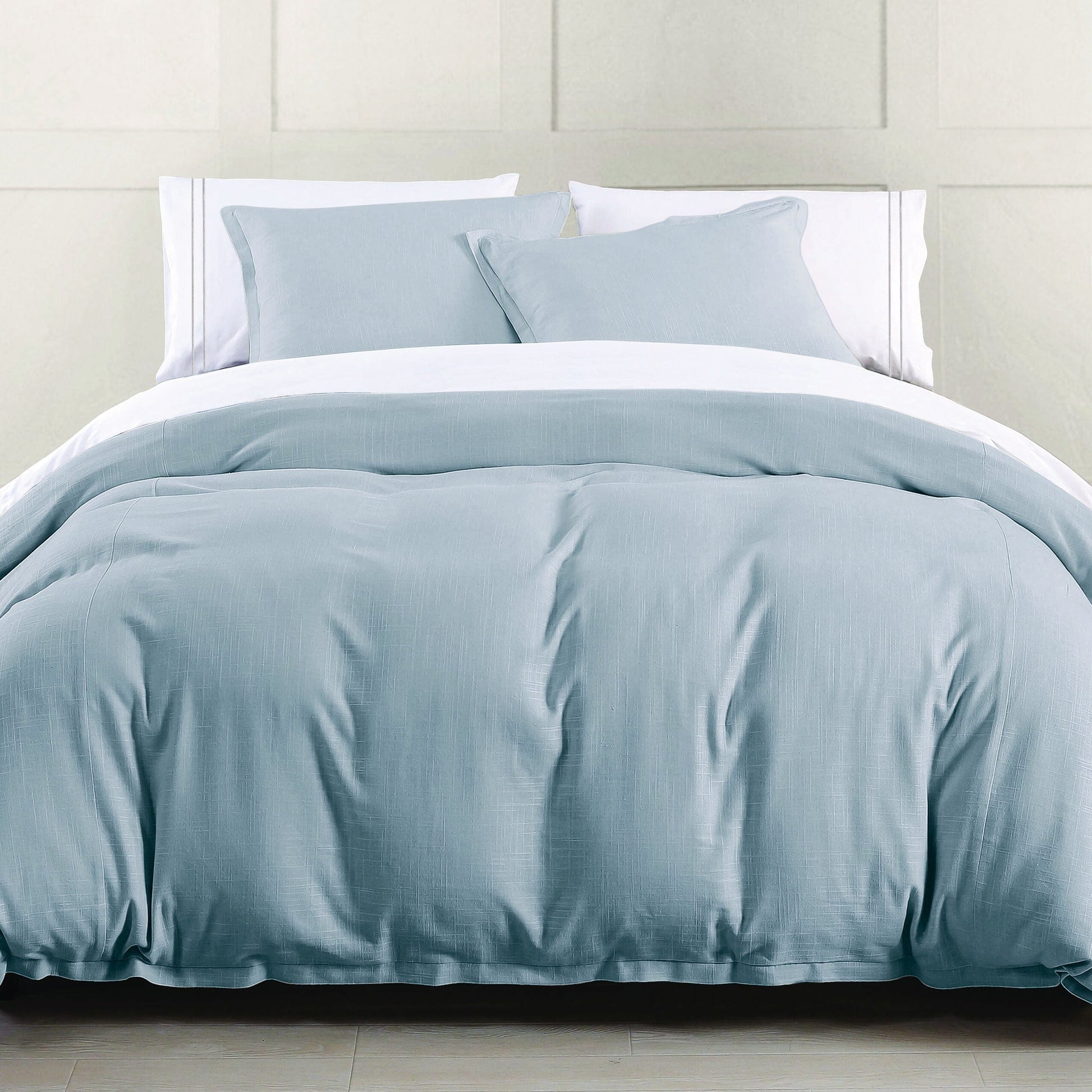 Blue comforter set on a bed with white pillows against a light gray wall.