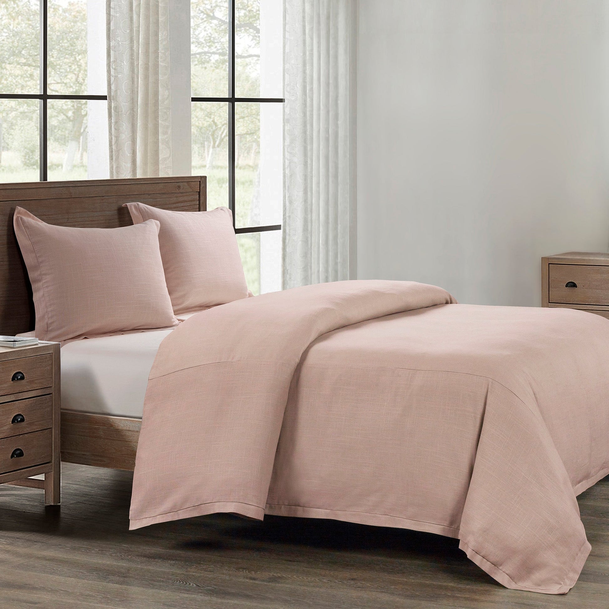 Bed with pink bedding and pillows in a room with large windows and light-colored walls.