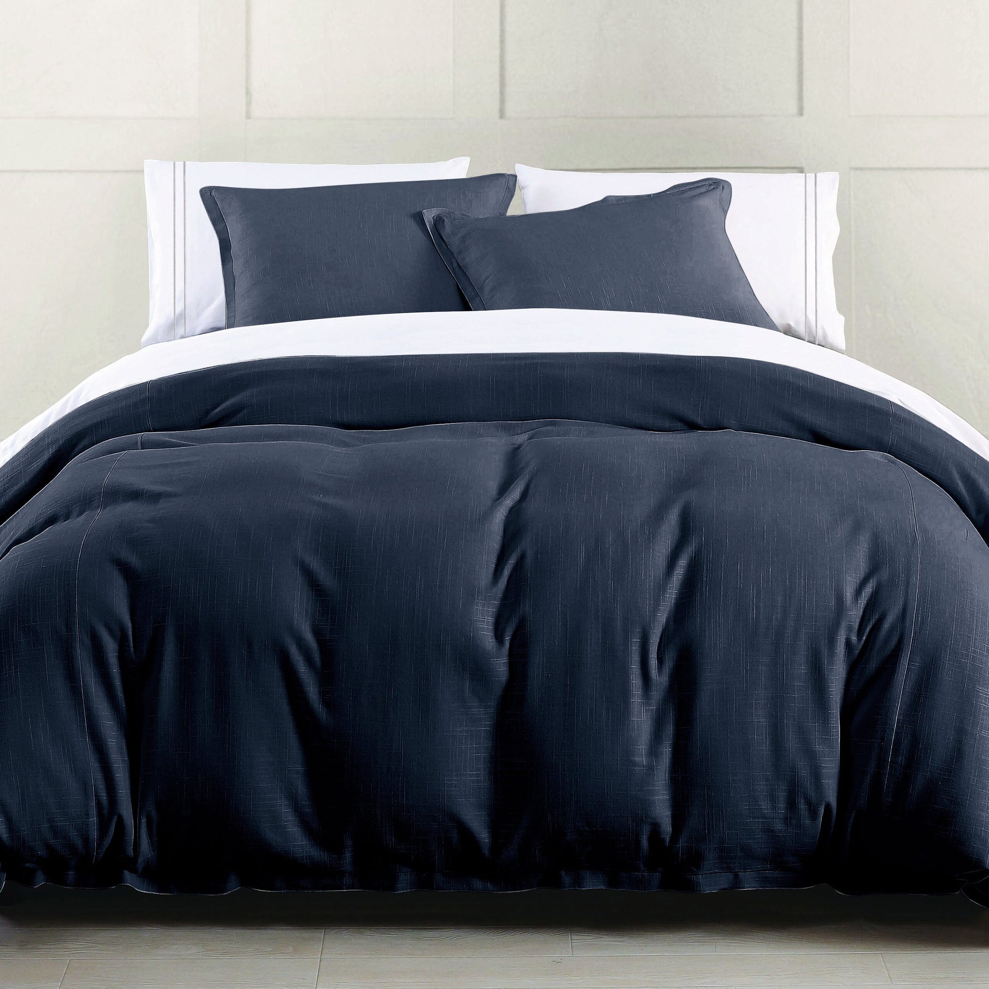 Navy blue comforter set on a bed with white pillows against a neutral wall.