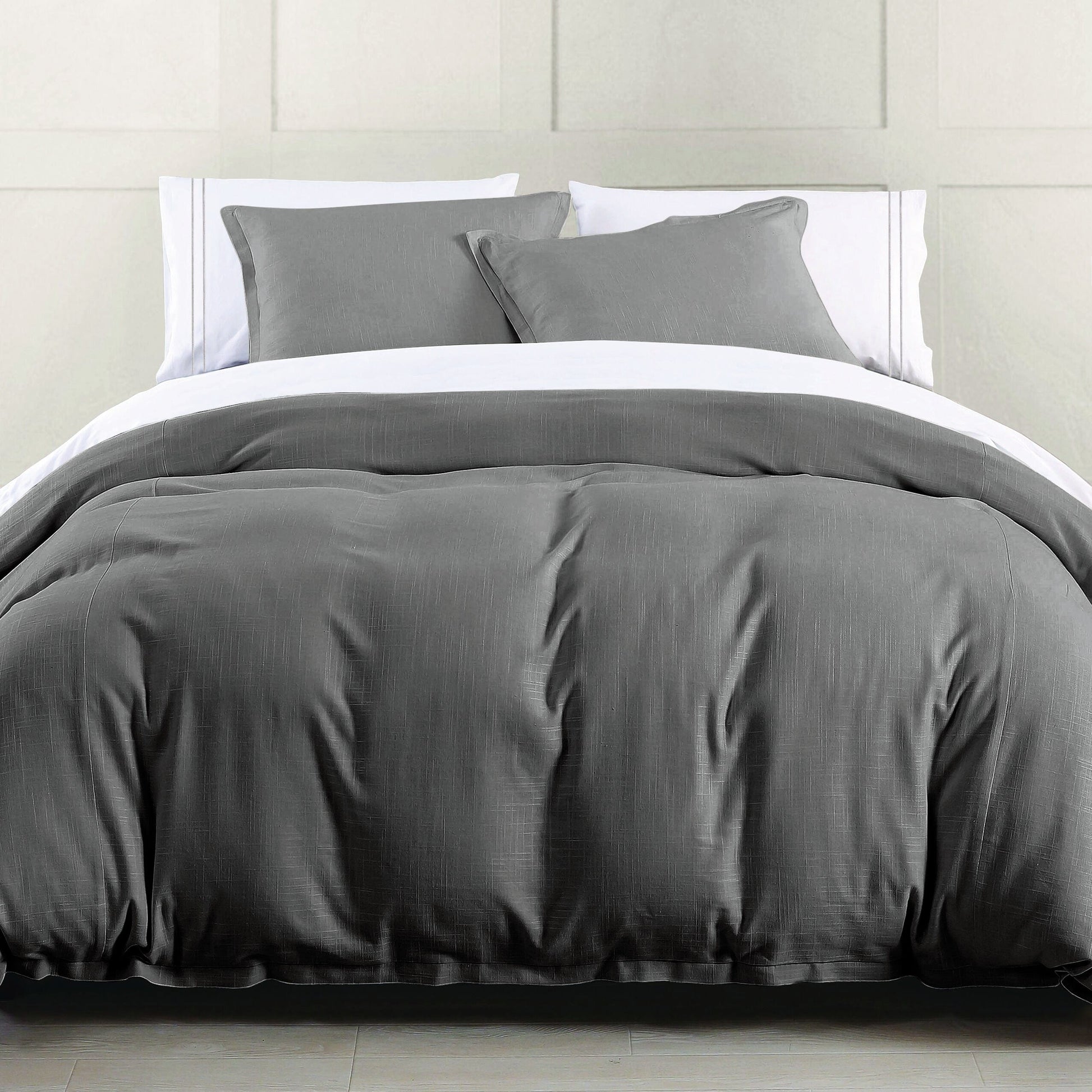 Gray bedding set on a bed with white pillows against a light gray wall.