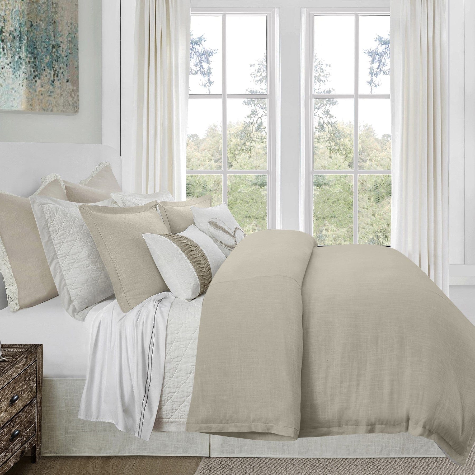 Neatly made bed with beige and white bedding in a bright bedroom.