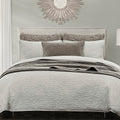 Neatly made bed with gray bedding and decorative pillows in a bedroom setting.