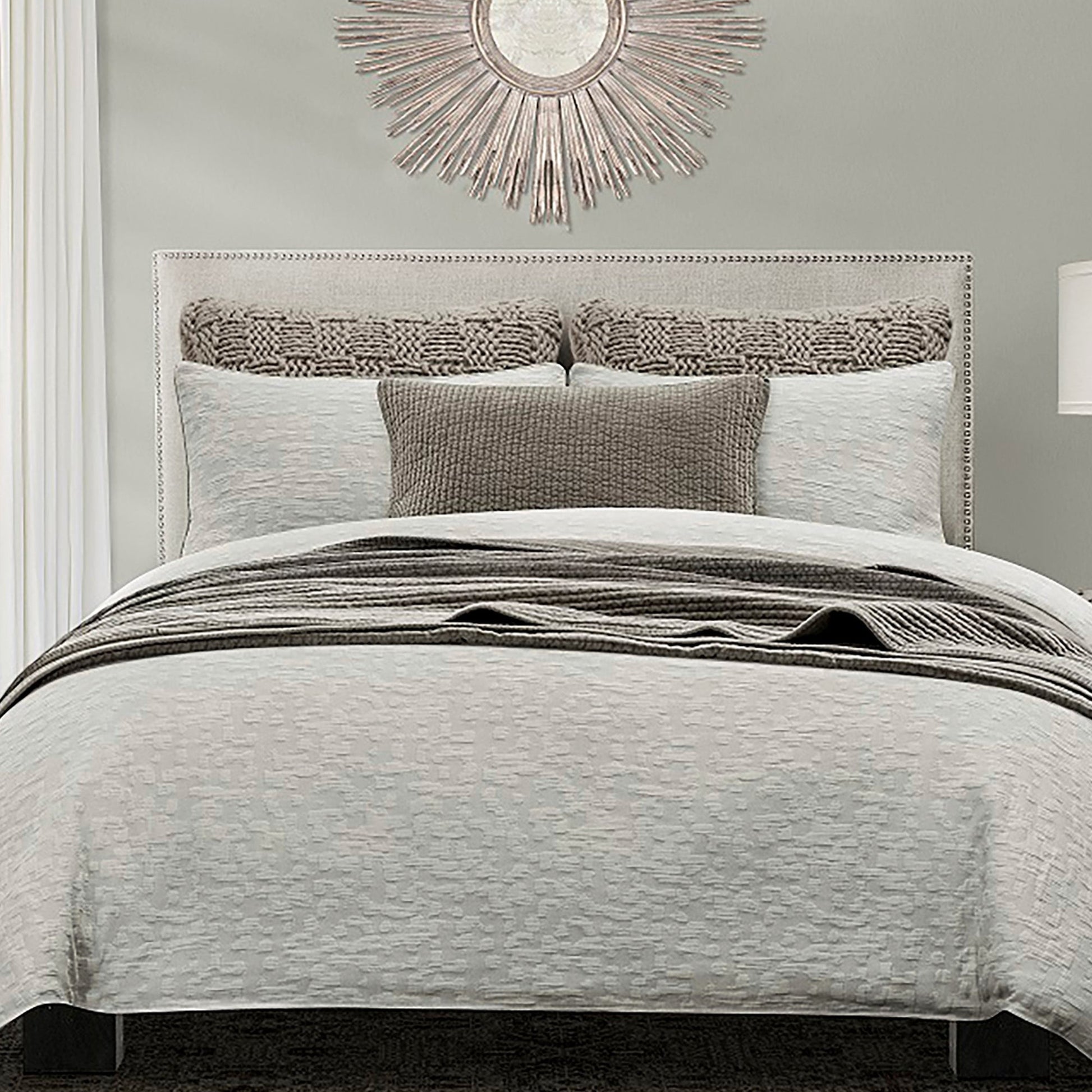 Neatly made bed with gray bedding and decorative pillows in a bedroom setting.