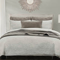 Neatly made bed with gray bedding and decorative pillows in a bedroom setting.