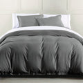 Gray bedding set on a bed with white pillows against a light gray wall.
