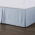 Light blue bedskirt on a bed against a wooden floor.