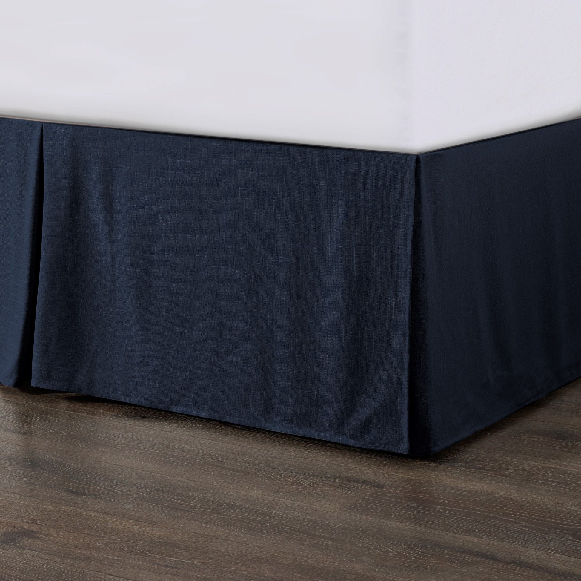 Navy blue bed skirt on a bed with a white mattress against a wooden floor.