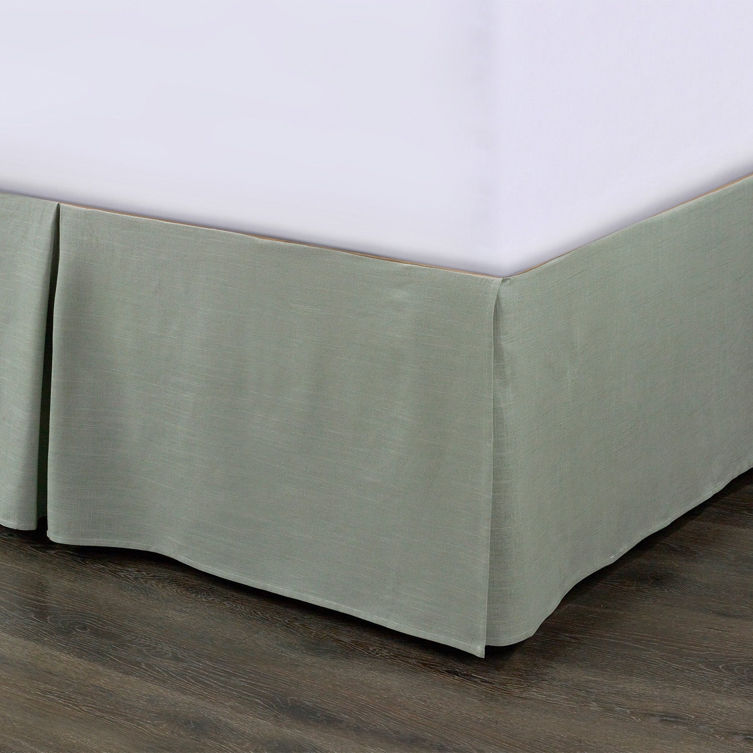 Green bed skirt on a bed with a white mattress against a neutral background