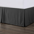 Dark gray bed skirt on a bed with white sheets against a wooden floor.