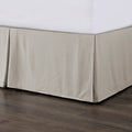 Beige bed skirt on a bed with white sheets against a wooden floor.