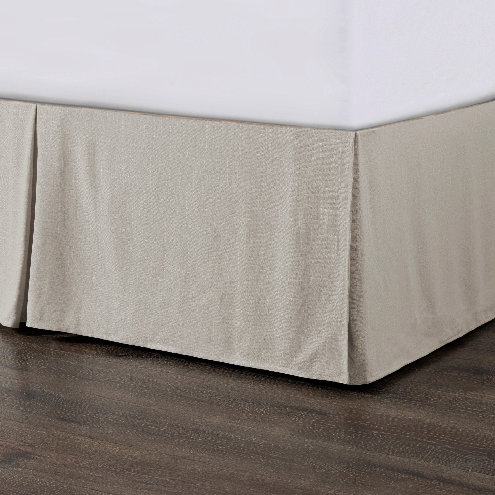 Beige bed skirt on a bed with white sheets against a wooden floor.