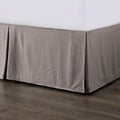 Gray bed skirt on a bed with a wooden floor.