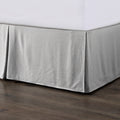 Gray bed skirt on a bed with a white mattress against a wooden floor.