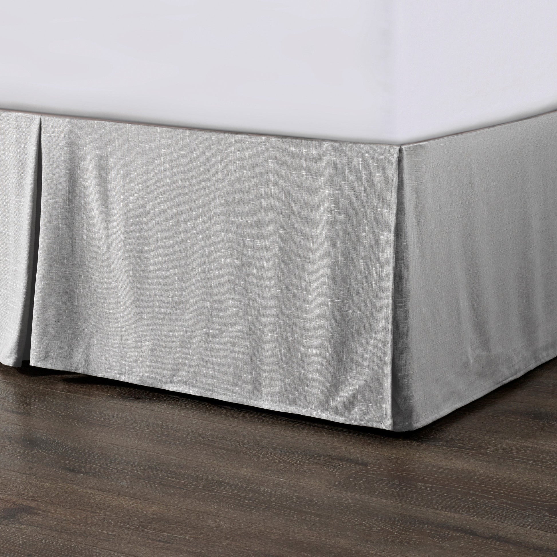 Gray bed skirt on a bed with a white mattress against a wooden floor.