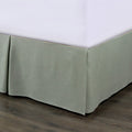 Green bed skirt on a bed with a white mattress against a neutral background