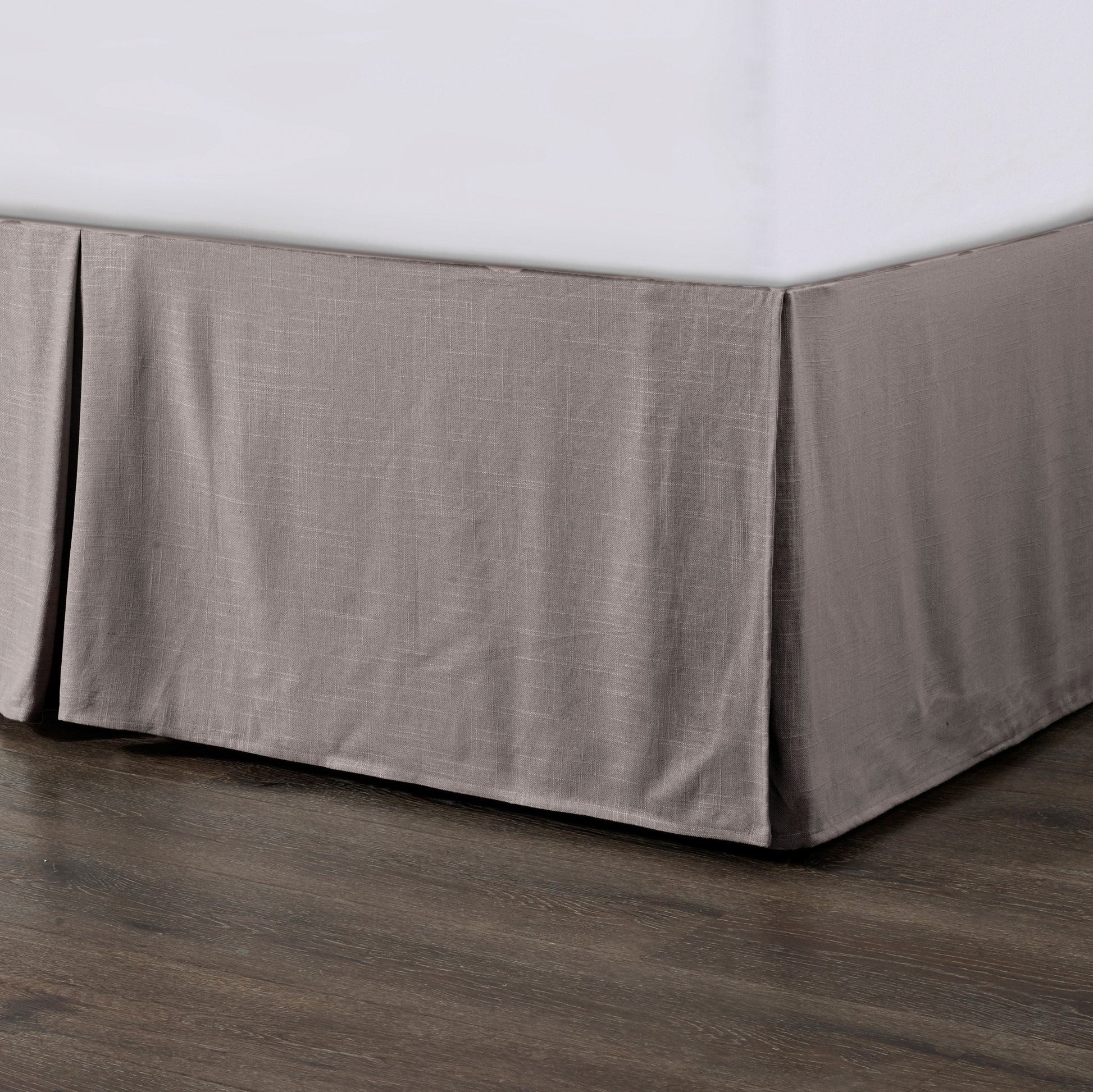 Gray bed skirt on a bed with a wooden floor.