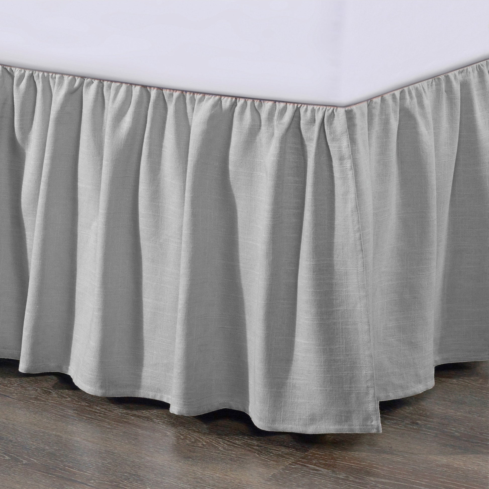 Gray bed skirt on a bed with a wooden floor and white wall in the background
