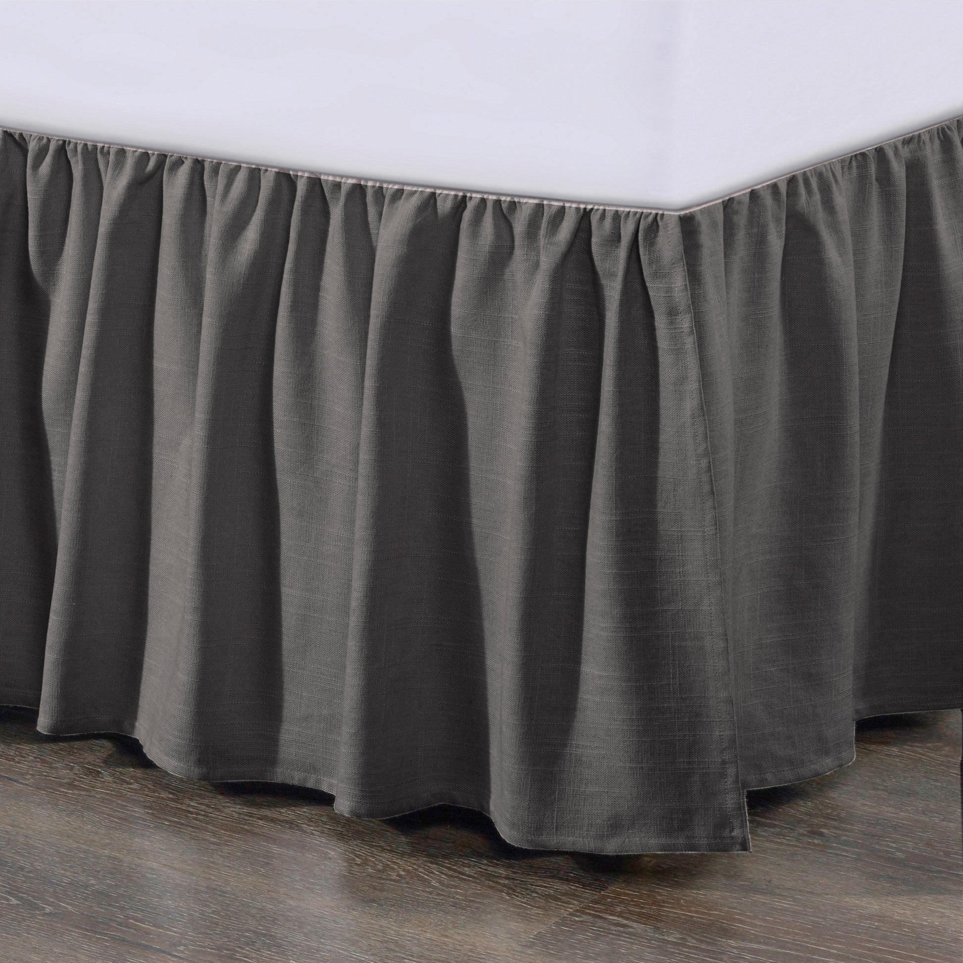 Gray bed skirt on a bed with a white mattress against a wooden floor.