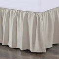 Beige bed skirt on a bed with a wooden floor and white wall background