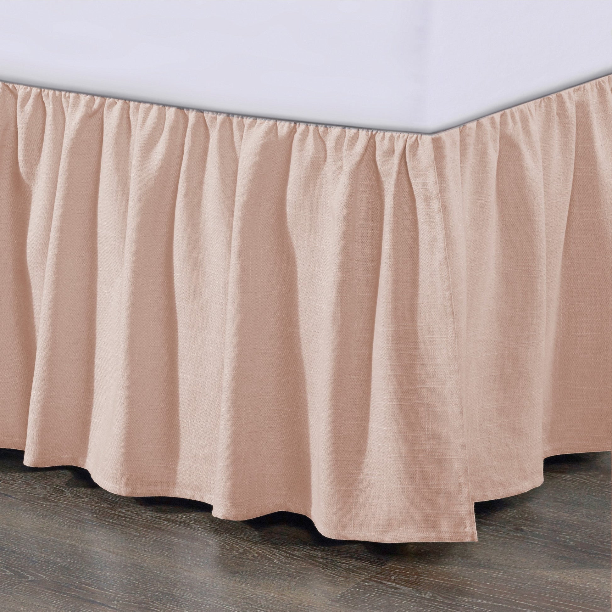 Pink bedskirt on a bed with a wooden floor and white wall background