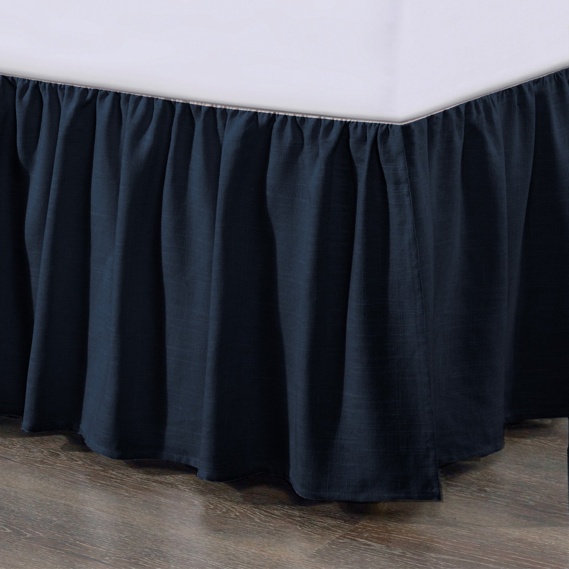 Dark blue bed skirt on a bed with a wooden floor.
