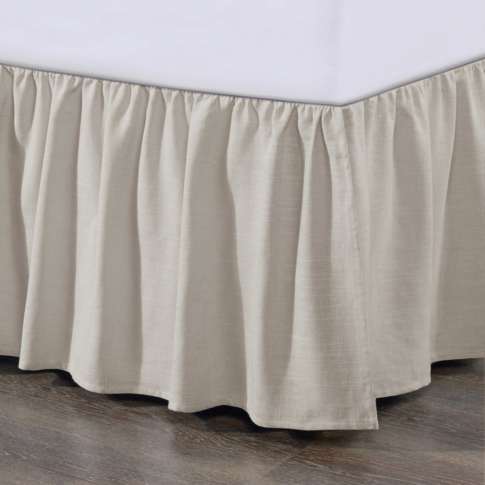 Beige bed skirt on a bed with a wooden floor and white wall background