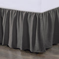 Gray bed skirt on a bed with a white mattress against a wooden floor.