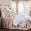 Neatly made bed with pink bedding and white ruffled blanket in a bright bedroom.