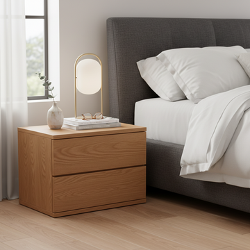 Wooden nightstand with a lamp and decor items next to a bed in a bedroom.