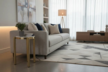 Modern living room with a gray sofa, noan white and gold side table, and decorative elements.