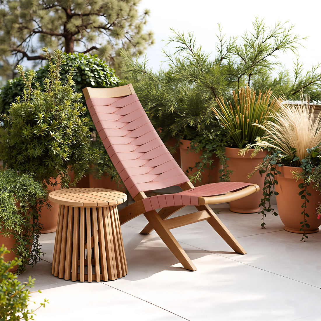 Pink outdoor lounge chair with wooden legs and a matching zahara side table natural on a patio with plants.